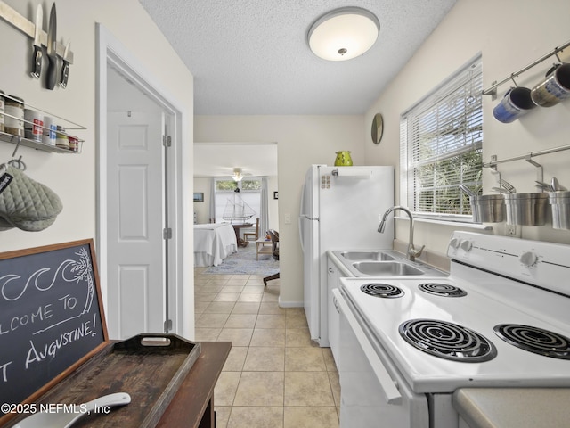 kitchen featuring a sink, white appliances, light tile patterned floors, and a textured ceiling