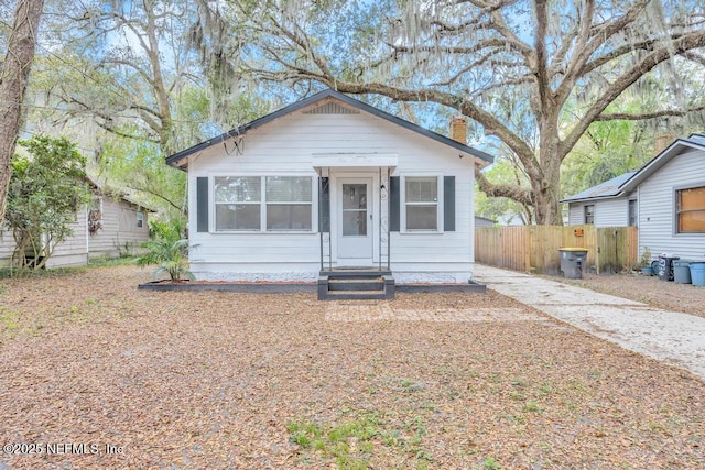 bungalow with entry steps, a chimney, and fence