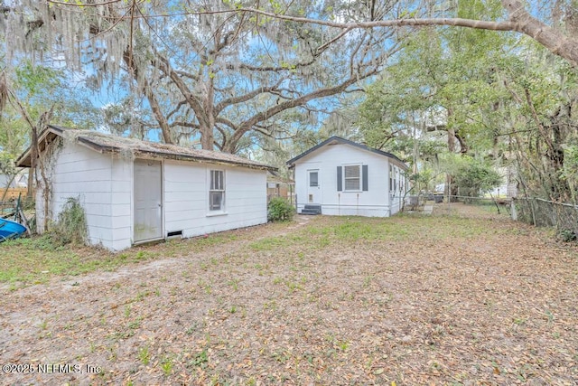 rear view of property featuring an outdoor structure and fence