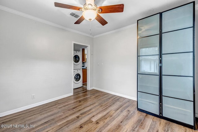 unfurnished room with wood finished floors, visible vents, baseboards, stacked washer / drying machine, and ornamental molding