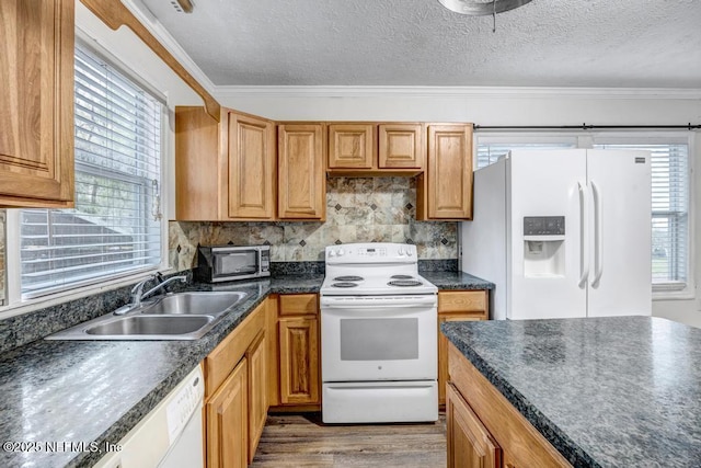 kitchen featuring white appliances, wood finished floors, a sink, dark countertops, and crown molding