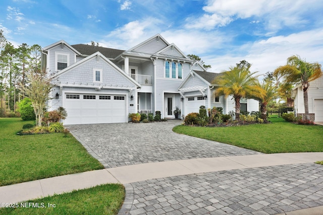 view of front of house featuring a front yard, decorative driveway, a balcony, and an attached garage