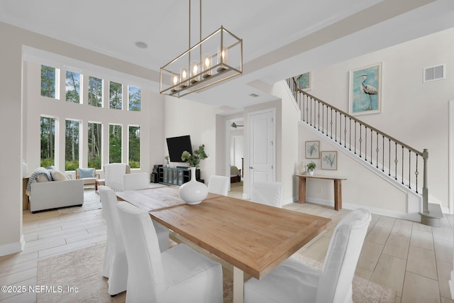 dining area with a notable chandelier, visible vents, a towering ceiling, wood tiled floor, and stairs