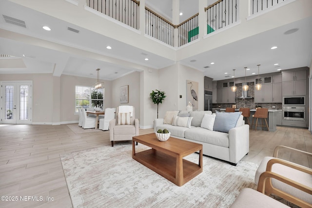 living area featuring light wood-type flooring, baseboards, a high ceiling, and visible vents