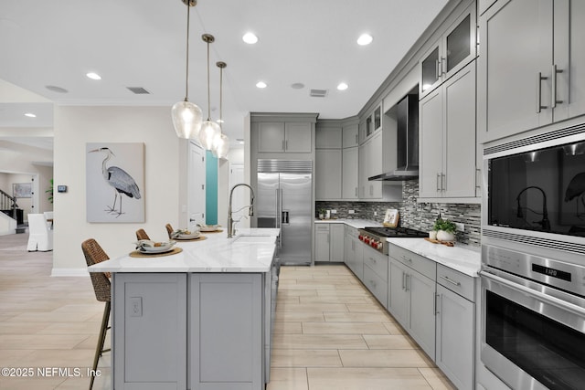 kitchen featuring built in appliances, wall chimney exhaust hood, backsplash, and gray cabinetry