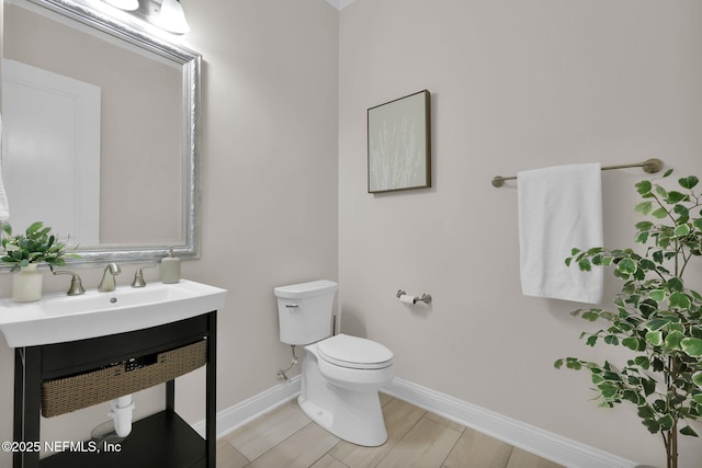 half bath with baseboards, vanity, toilet, and wood finished floors