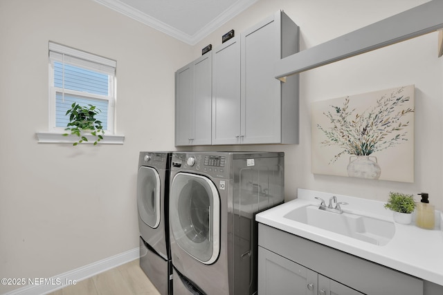 clothes washing area with a sink, ornamental molding, light wood-type flooring, independent washer and dryer, and cabinet space