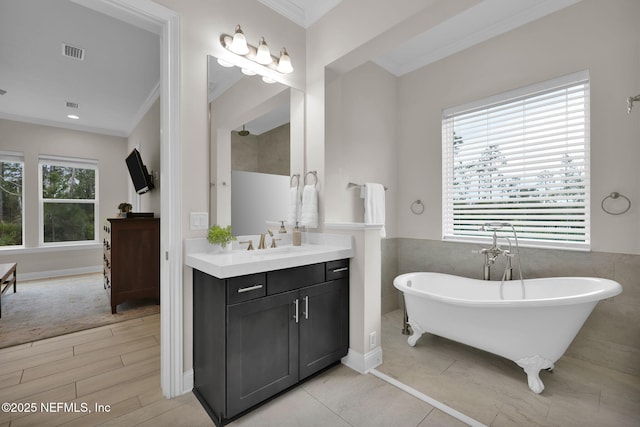 full bath featuring ornamental molding, a freestanding tub, visible vents, and vanity