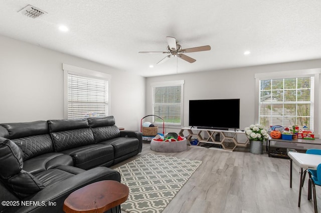 living area with ceiling fan, a textured ceiling, visible vents, and wood finished floors