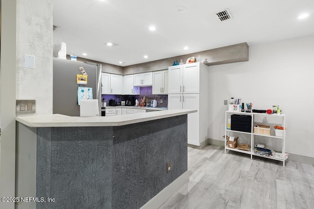 kitchen featuring freestanding refrigerator, a peninsula, light wood-type flooring, white cabinetry, and backsplash