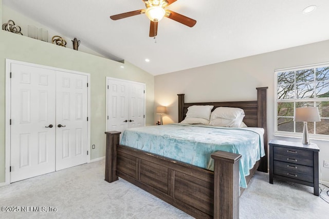 bedroom with ceiling fan, light colored carpet, baseboards, vaulted ceiling, and two closets