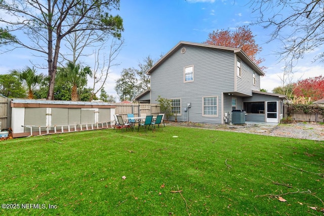 rear view of property with a yard, cooling unit, a fenced backyard, and a sunroom