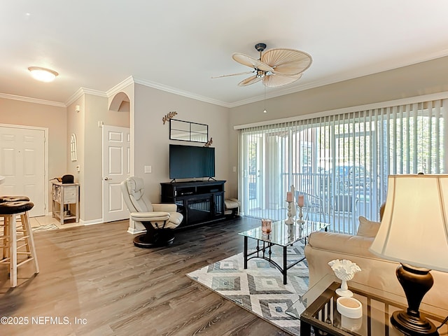 living area with ornamental molding, a ceiling fan, baseboards, and wood finished floors