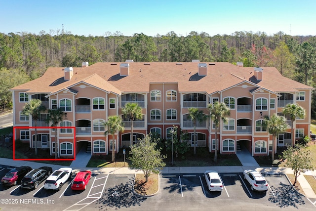 view of building exterior with uncovered parking and a view of trees