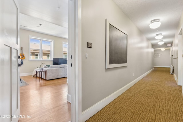 hallway with a textured ceiling, baseboards, and wood finished floors