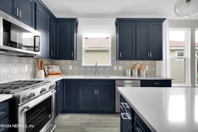 kitchen featuring stainless steel appliances, a sink, blue cabinetry, light wood-type flooring, and tasteful backsplash