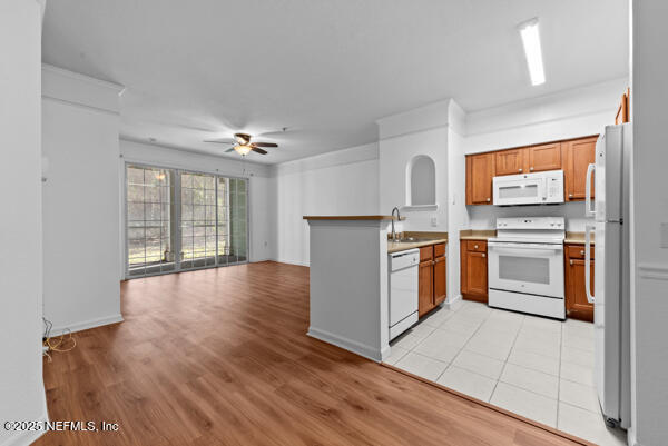 kitchen featuring brown cabinets, light wood-style flooring, open floor plan, white appliances, and a peninsula