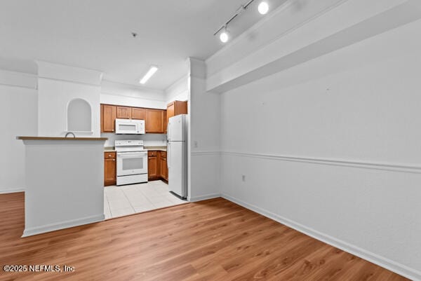 kitchen with white appliances, brown cabinets, a peninsula, light countertops, and light wood-type flooring