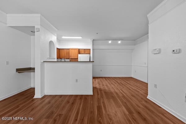 unfurnished living room with wood finished floors, rail lighting, and baseboards