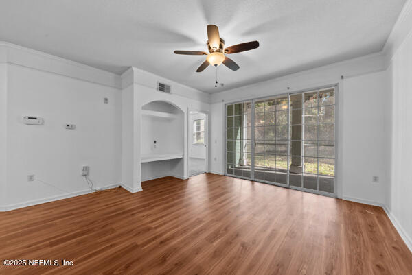 unfurnished living room featuring a ceiling fan, visible vents, arched walkways, and wood finished floors