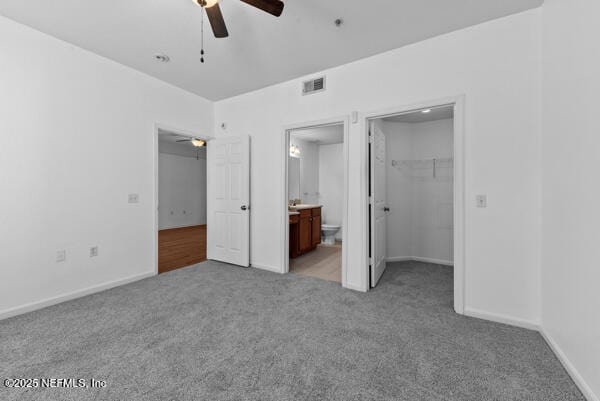 unfurnished bedroom with connected bathroom, light colored carpet, visible vents, a spacious closet, and a closet