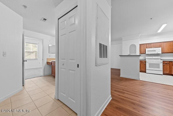 kitchen with light tile patterned floors, white appliances, visible vents, baseboards, and brown cabinetry