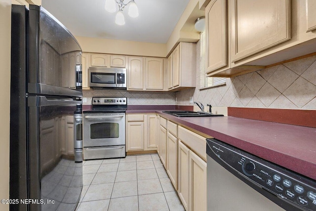 kitchen with stainless steel appliances, dark countertops, backsplash, light tile patterned flooring, and a sink