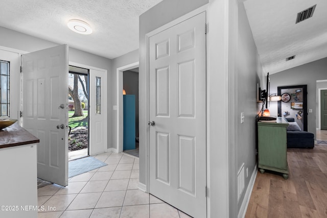 entrance foyer with lofted ceiling, visible vents, light tile patterned flooring, a textured ceiling, and baseboards