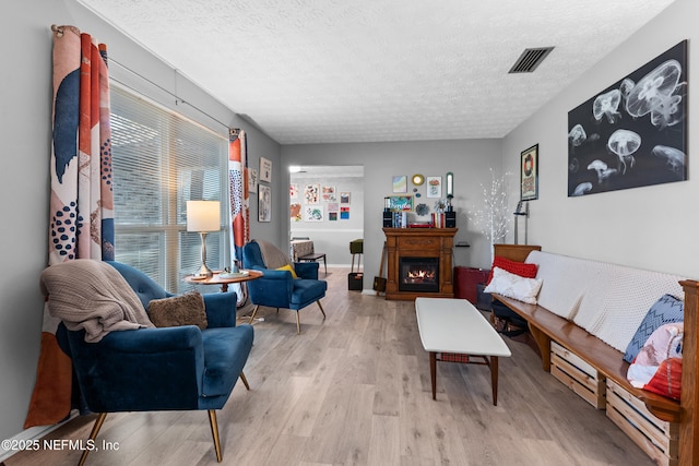 living area featuring a textured ceiling, a baseboard heating unit, wood finished floors, visible vents, and a lit fireplace