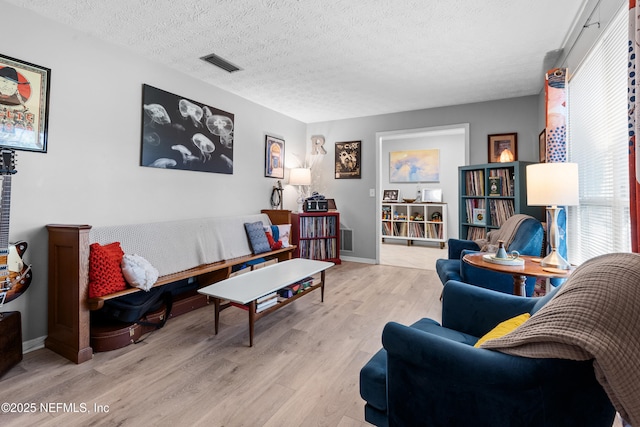 living area featuring a textured ceiling, wood finished floors, visible vents, and baseboards