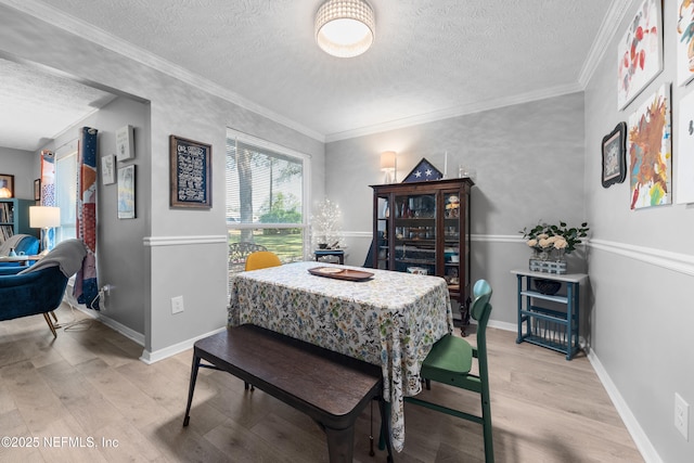 dining area with light wood-style floors, baseboards, a textured ceiling, and ornamental molding