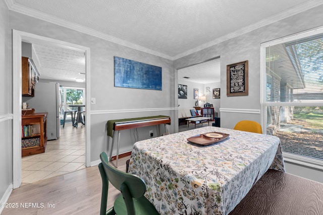 dining space with light wood-type flooring, crown molding, a textured ceiling, and baseboards