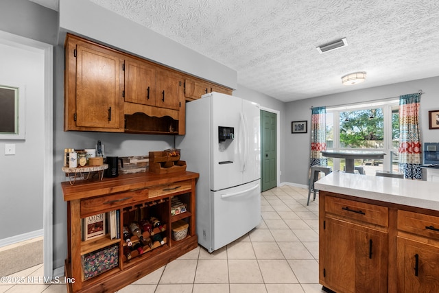 kitchen featuring visible vents, brown cabinetry, light countertops, white fridge with ice dispenser, and light tile patterned flooring