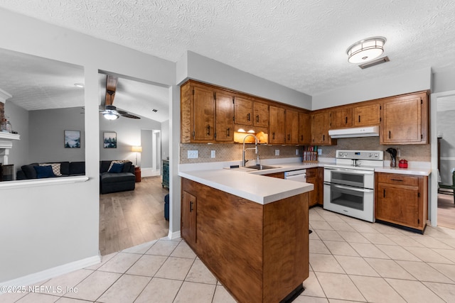 kitchen with white appliances, light tile patterned floors, a peninsula, under cabinet range hood, and a sink