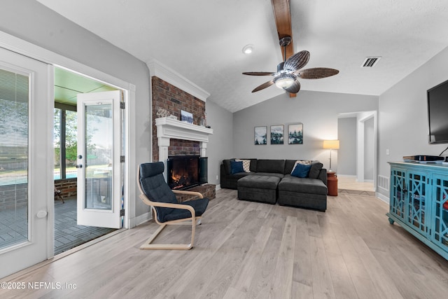 living area with lofted ceiling with beams, wood finished floors, visible vents, a ceiling fan, and a brick fireplace