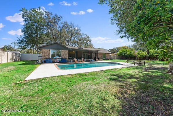 back of property with a fenced backyard, brick siding, a yard, a fenced in pool, and a patio area