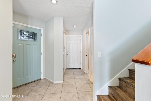 entryway with light tile patterned floors, stairway, a textured ceiling, and baseboards