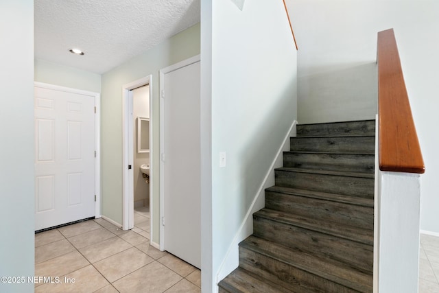 stairway with tile patterned floors, baseboards, and a textured ceiling