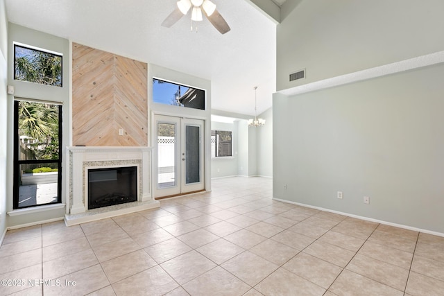 unfurnished living room featuring tile patterned flooring, visible vents, ceiling fan with notable chandelier, a fireplace, and a towering ceiling