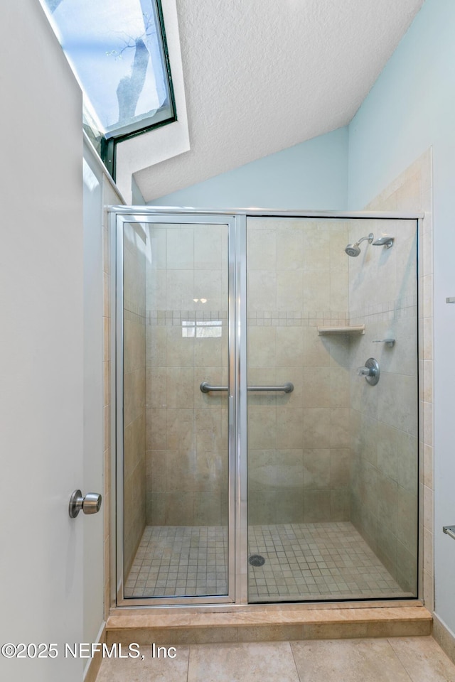 bathroom featuring tile patterned flooring, a shower stall, a textured ceiling, and vaulted ceiling