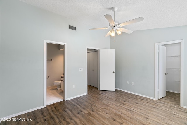 unfurnished bedroom featuring a spacious closet, visible vents, vaulted ceiling, wood finished floors, and a textured ceiling