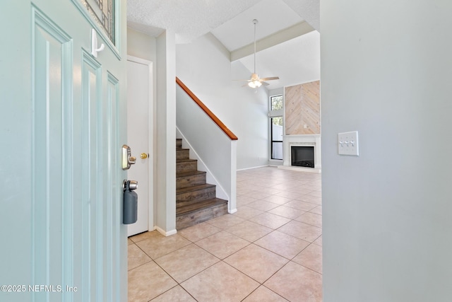 foyer with light tile patterned floors, a fireplace, stairs, and ceiling fan