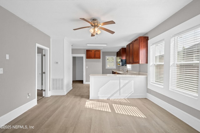 kitchen featuring baseboards, a ceiling fan, light countertops, light wood-style floors, and a sink