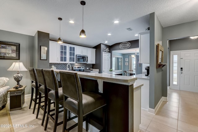 kitchen with visible vents, a peninsula, stainless steel appliances, and glass insert cabinets