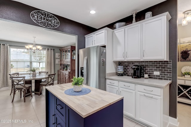 kitchen with decorative backsplash, white cabinets, wood counters, a notable chandelier, and stainless steel fridge