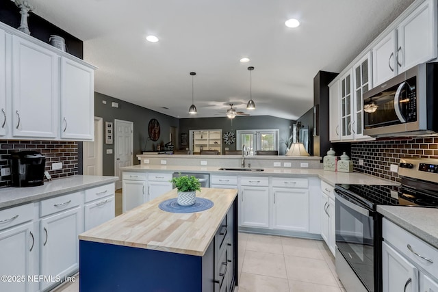 kitchen featuring light tile patterned floors, a peninsula, a sink, butcher block countertops, and stainless steel appliances