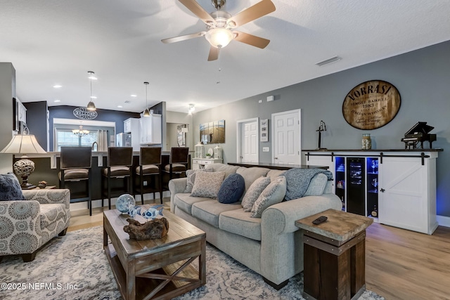 living room featuring visible vents, beverage cooler, ceiling fan with notable chandelier, light wood finished floors, and lofted ceiling