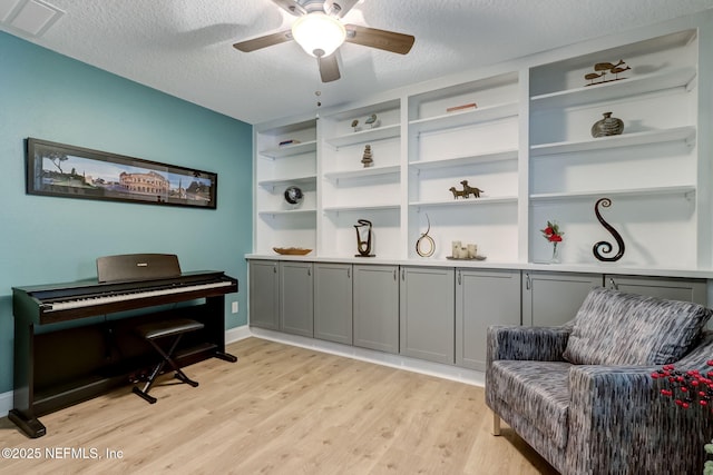 living area with a ceiling fan, baseboards, visible vents, light wood-style flooring, and a textured ceiling