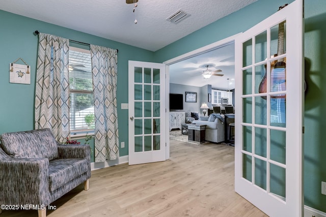 living area featuring a ceiling fan, wood finished floors, visible vents, french doors, and a textured ceiling