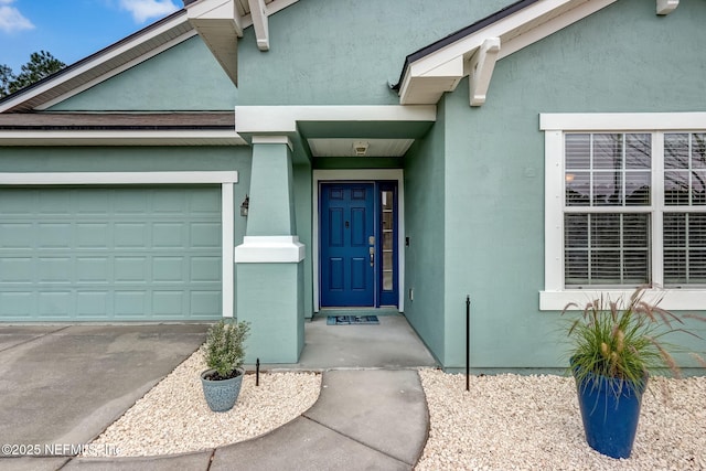 view of exterior entry with stucco siding, a garage, and driveway